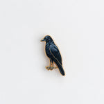 American crow enamel pin with a gold edge and deep blue iridescent body on a white background