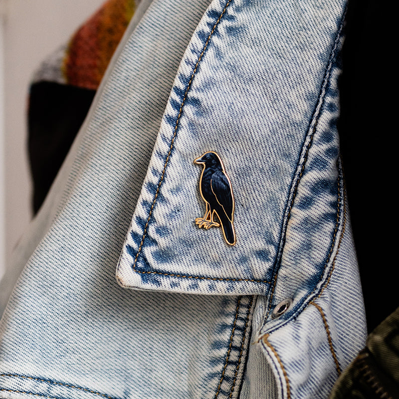 American Crow enamel pin with a gold edge attached to light wash denim jacket