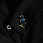 Blue crow enamel pin with a gold edge on a black jacket