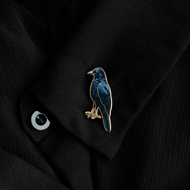 Blue crow enamel pin with a gold edge on a black jacket
