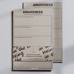 Front view of the Awareness notepad set with stacked sheets and a decorative wraparound band