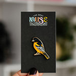Baltimore Oriole enamel pin with vivid orange and black plumage mounted on a black display card.