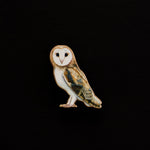 Barn Owl enamel pin centered on a black background with a white face and brown tan body.