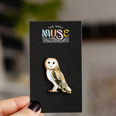 Barn owl enamel pin with white face and speckled brown body mounted on black display card with The Gray Muse logo