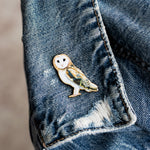 Barn Owl enamel pin attached to a blue denim jacket, featuring a heart shaped face and pale plumage.