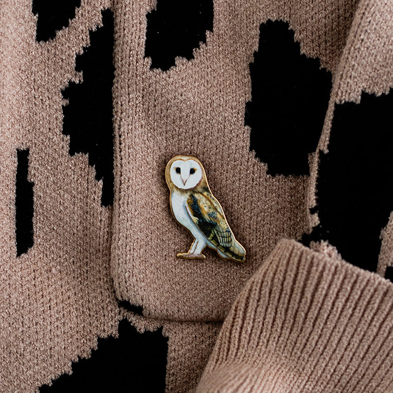 Barn Owl enamel pin attached to a brown knit sweater with a black pattern.