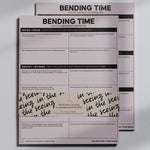 Two pink Bending Time Notepad booklets stacked with bold BENDING TIME title and grid prompts for reflection
