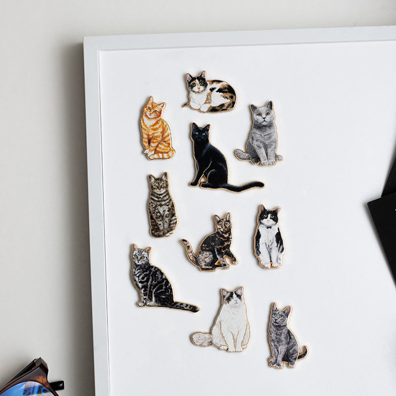 Cat enamel pins displayed on a white board in a neat cluster showcasing a variety of cat designs