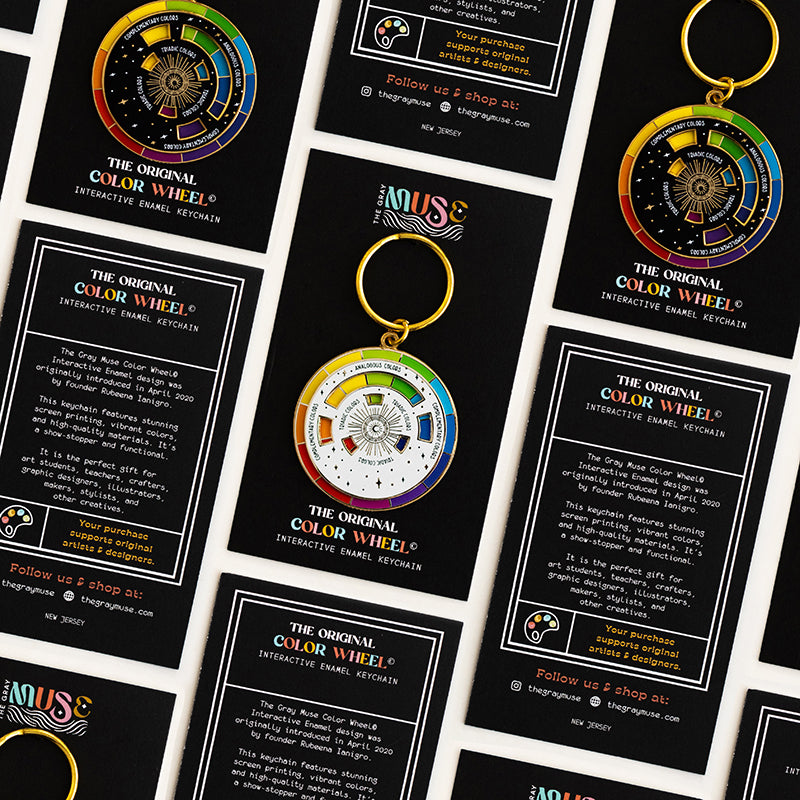 Grid layout of Color Wheel packaging cards and enamel keychains arranged on a pale surface to show gift bundle options.