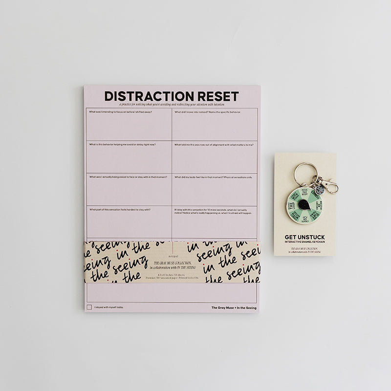 Distraction Reset bundle shown with a purple notepad, a Get Unstuck spinner keychain, and decorative wrap on a light desk.