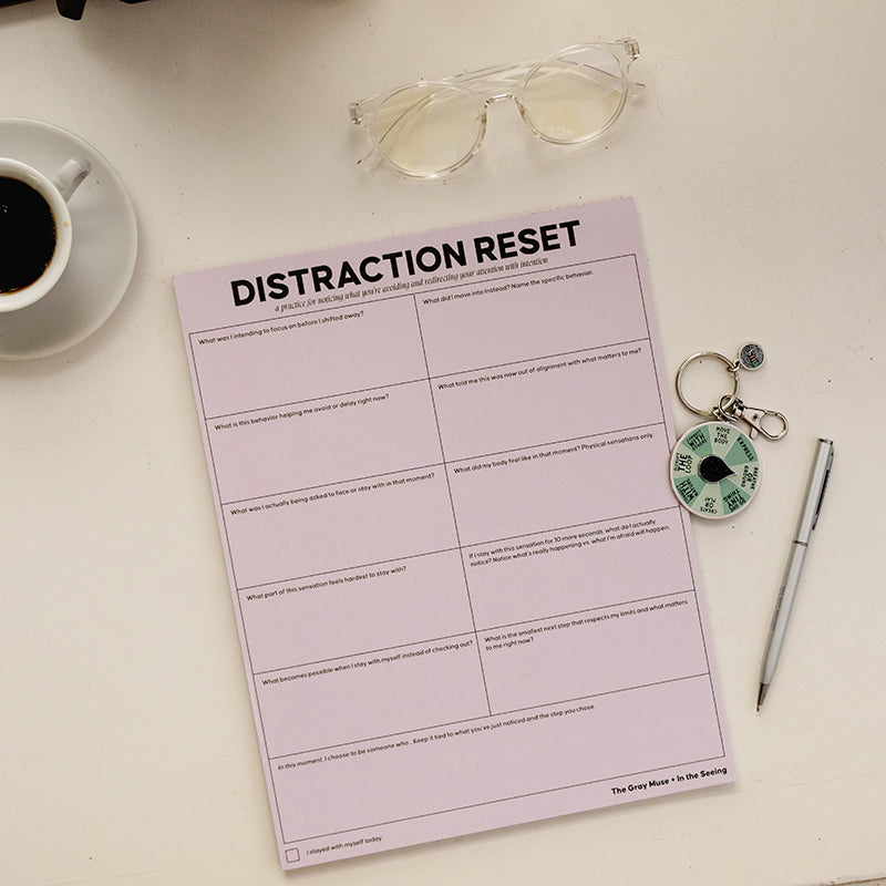 Top view of a pink DISTRACTION RESET notepad with coffee, glasses, and a spinner keychain.