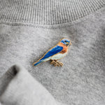 Eastern bluebird enamel pin attached to gray knit sweater fabric.