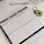 Energetic Capacity Bundle on a white desk with the Energy Leaks Tracker notepad, a silver pen, and a green spinner keychain.