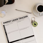 Energy Leaks Tracker notepad displayed from above with a coffee cup nearby and a round spinner keychain beside.