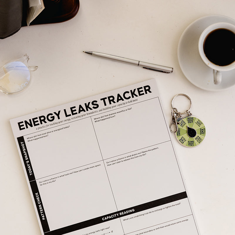 Energy Leaks Tracker notepad displayed from above with a coffee cup nearby and a round spinner keychain beside.