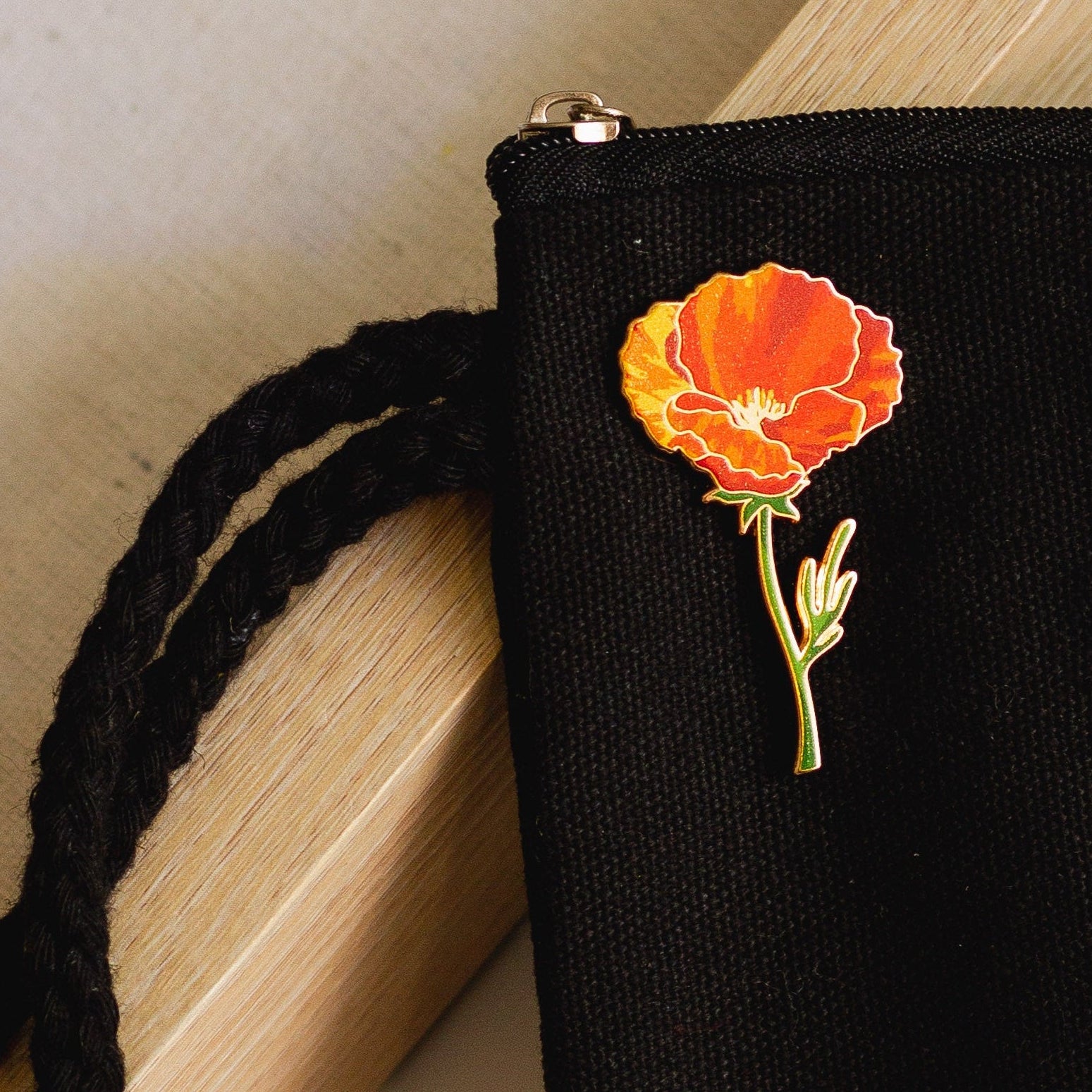 Orange California poppy enamel pin on a dark display card resting on a black textured bag