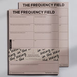 Two pink The Frequency Field Notepads stacked with bold title at top and a grid prompt layout visible.