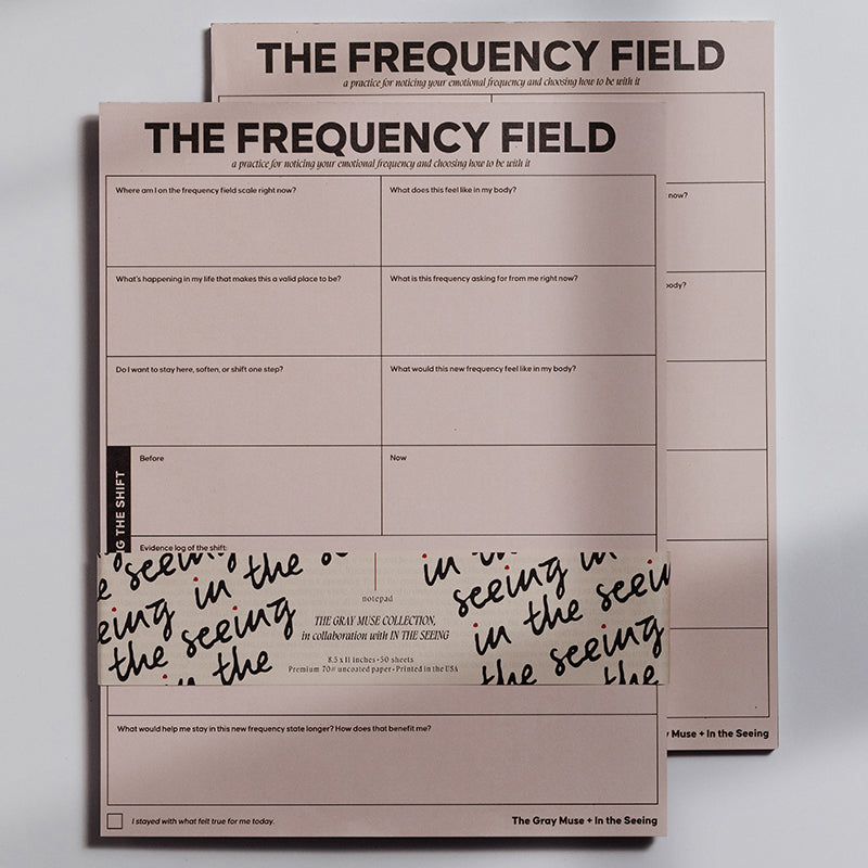 Two pink The Frequency Field Notepads stacked with bold title at top and a grid prompt layout visible.