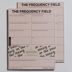 Two pink The Frequency Field Notepads stacked together showing bold title and grid pages for emotional frequency tracking.