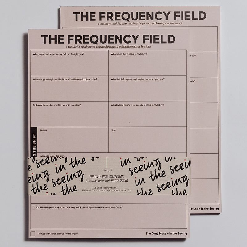 Two pink The Frequency Field Notepads stacked together showing bold title and grid pages for emotional frequency tracking.