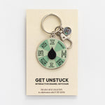 Get Unstuck interactive enamel keychain with a mint green segmented wheel and black center on a display card.