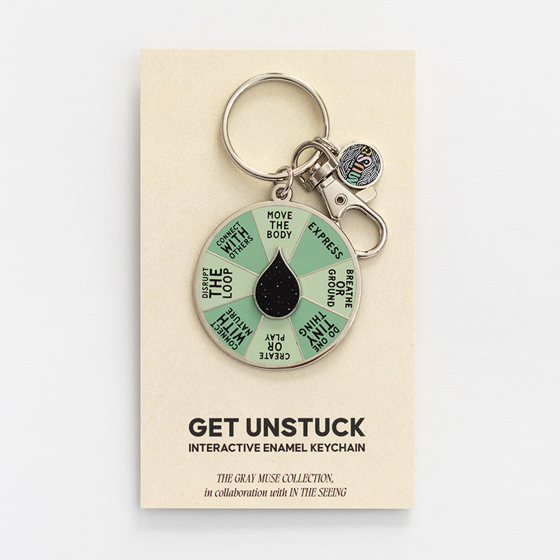 Get Unstuck interactive enamel keychain with a mint green segmented wheel and black center on a display card.