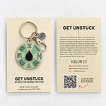 Flat lay of Get Unstuck spinner enamel keychain with beige packaging cards on a neutral background