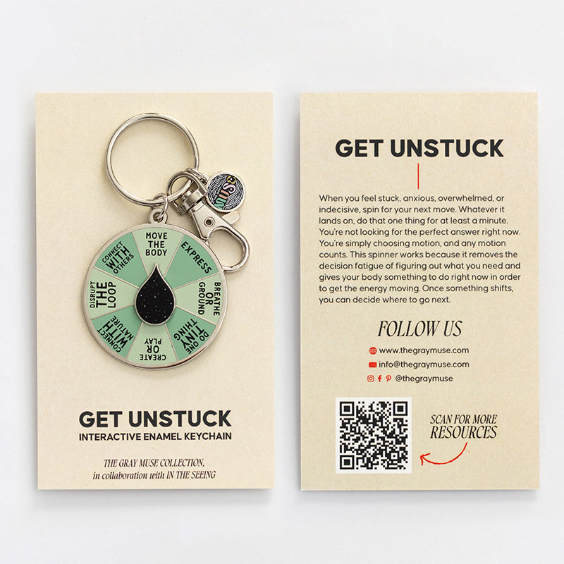 Flat lay of Get Unstuck spinner enamel keychain with beige packaging cards on a neutral background