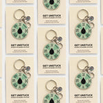 Grid of Get Unstuck enamel keychains on beige cards displayed as product collection
