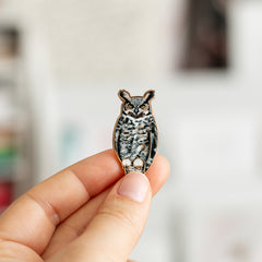 Great Horned Owl enamel pin held between fingers against a black background.