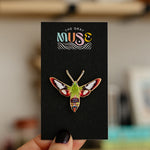 Hummingbird Clearwing Moth enamel pin on a black display card with a green body and red wing accents