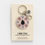 I See You Spinner Interactive Enamel Keychain on a beige display card with a pink affirmation wheel and a black teardrop centerpiece