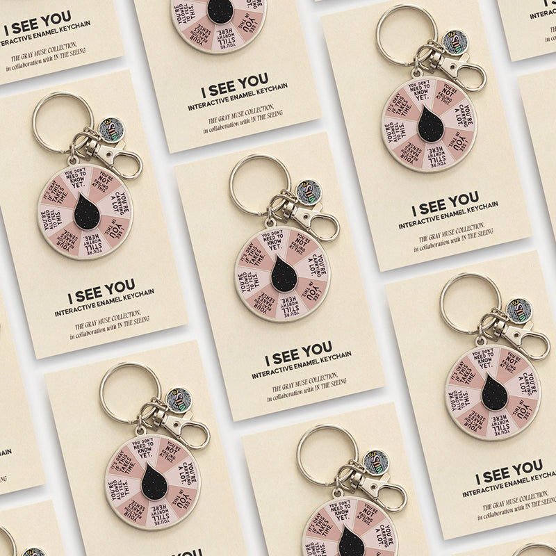 Assorted I See You spinner enamel keychains on beige display cards.