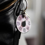 Close up of I See You Spinner Interactive Enamel Keychain attached to a black bag, showing a pink affirmation wheel and a colorful circular charm
