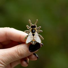 Hand holding a 1.25 inch European Honey Bee enamel pin with black and yellow stripes.