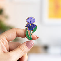 Purple bearded iris enamel pin with green leaves held between fingers