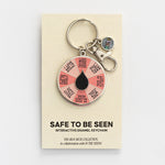 It's Safe to Be Seen spinner enamel keychain displayed on a beige card.
