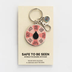 It's Safe to Be Seen spinner enamel keychain displayed on a beige card.