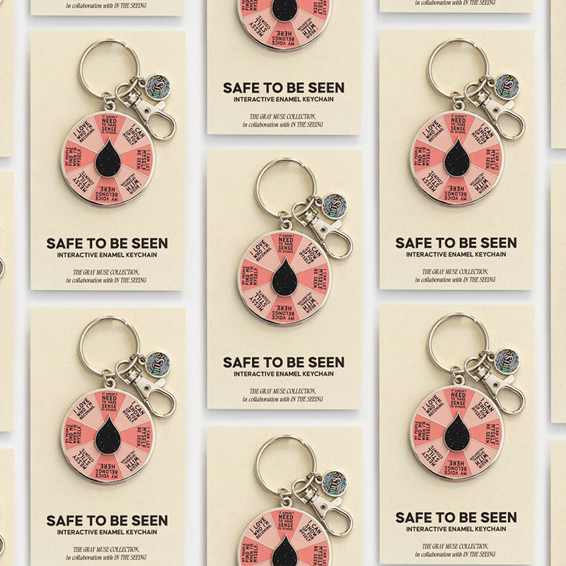 Grid of Safe to Be Seen spinner enamel keychains on beige display cards, each with a pink segmented wheel and a black teardrop center.