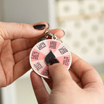 Hand holds a pink segmented spinner enamel keychain with a black teardrop center.