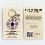 Two panel display featuring a round lavender spinner enamel keychain with a black teardrop center on a beige card
