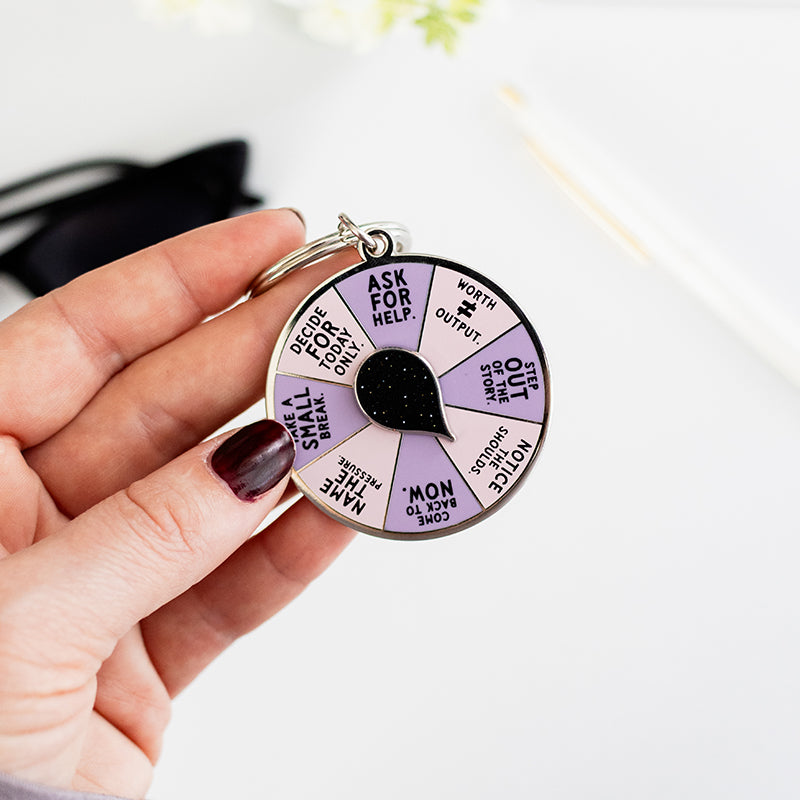 Hand holds the Safe to Release Pressure spinner enamel keychain showing the pastel purple segmented wheel
