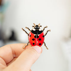 Ladybug enamel pin held between fingers with a red shell and black spots