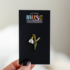 Snowdrop enamel pin with white petals and green stem mounted on a black display card