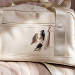 Beige bag with three bird enamel pins attached to the front pocket