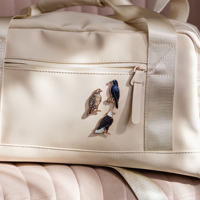 Beige bag with three bird enamel pins attached to the front pocket