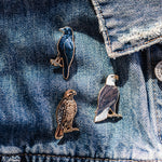 Three bird enamel pins attached to blue denim jacket fabric