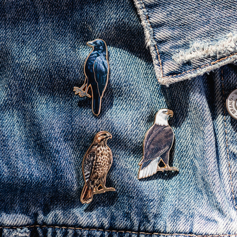 Three bird enamel pins attached to blue denim jacket fabric