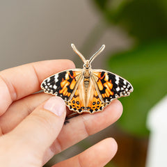 2-inch Painted Lady butterfly enamel pin with orange, black, and white wings held between fingers