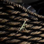 Praying mantis enamel pin with a green body and gold outline resting on a braided coiled rope background